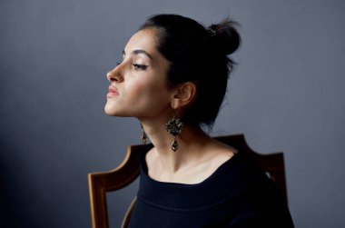 Sandalyeye oturmuş, makyaj küpeleri takmış güzel bir kadın manken.