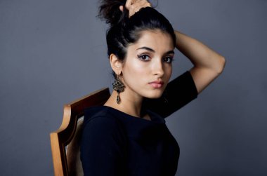 Sandalyeye oturmuş, makyaj küpeleri takmış güzel bir kadın manken.