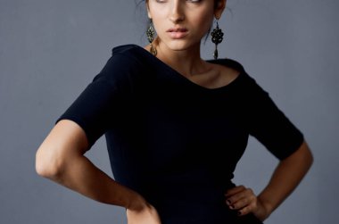  Siyah elbiseli kadın, gri arka planda el kol hareketi yapıyor. 