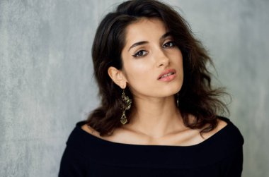 Gece makyajlı seksi bir kadın ve arka planda gri bir portrede küpeli şık bir kadın.