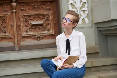 Elinde not defteri olan güzel bir kadın enstitü binasının yakınındaki merdivenlerde oturuyor.