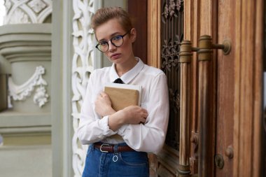 Güzel kadın model kot pantolon. Elinde kitap var. Caddeye yakın bina.