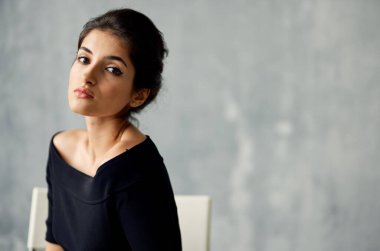 Gri arka plan ve açık renk koltuklu çekici bir kadının portresi.