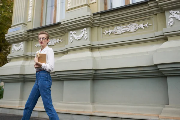 Güzel kadın model kot pantolon. Elinde kitap var. Caddeye yakın bina.