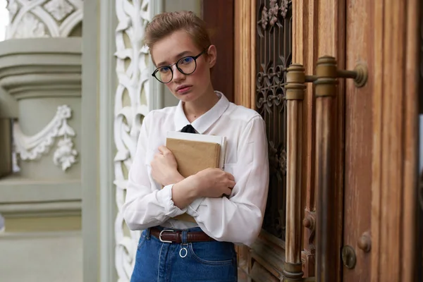 Güzel kadın model kot pantolon. Elinde kitap var. Caddeye yakın bina.