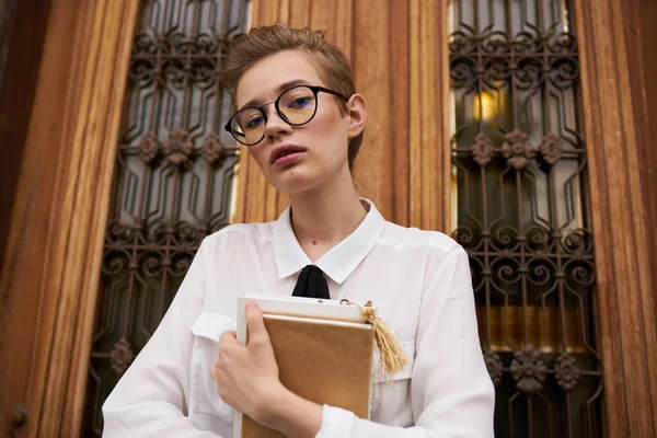 Студентка в очках с книгой в руках у высоких дверей учебного заведения — стоковое фото
