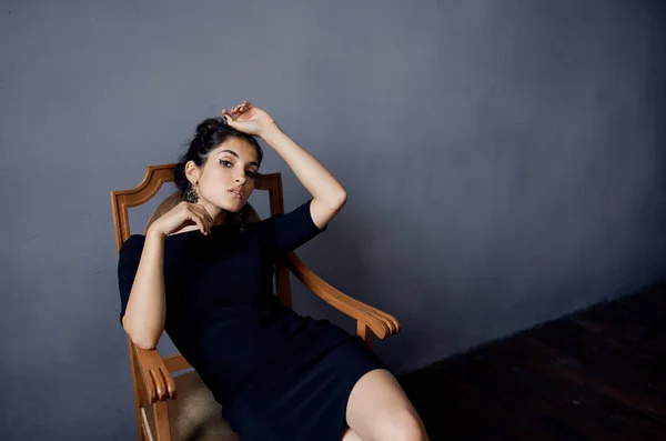 Atractiva dama en vestido se sienta en la silla en el interior y la pared gris —  Fotos de Stock