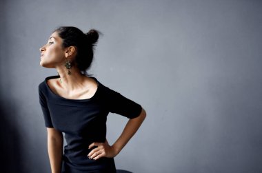 Gri arka planda siyah elbiseli zarif bir bayan. Kapalı alanda saç stili. El hareketleriyle mekanı kopyala.