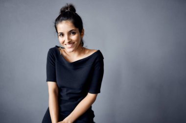 Gri arka planda siyah elbiseli zarif bir bayan. Kapalı alanda saç stili. El hareketleriyle mekanı kopyala.