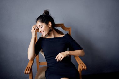 Siyah elbiseli zarif kadın gri odadaki tahta koltukta oturuyor.