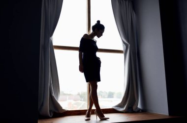 Pencere perdesi ve gri perde modelinde büyüyen bir kadının silüeti.