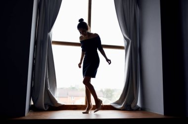 Pencere perdesi ve gri perde modelinde büyüyen bir kadının silüeti.