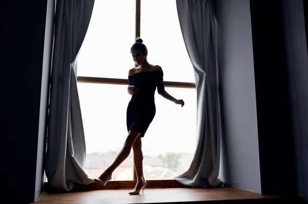 Silhouette d'une femme en pleine croissance sur un rebord de fenêtre et rideaux gris modèle — Photo