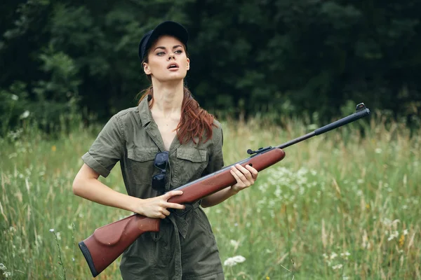 Mulher militar com armas na mão, um macacão verde olha para a tampa preta lateral — Fotografia de Stock