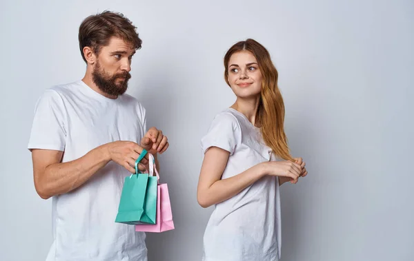 Ofendida mujer se alejó de un hombre con bolsas de regalo sobre un fondo claro — Foto de Stock