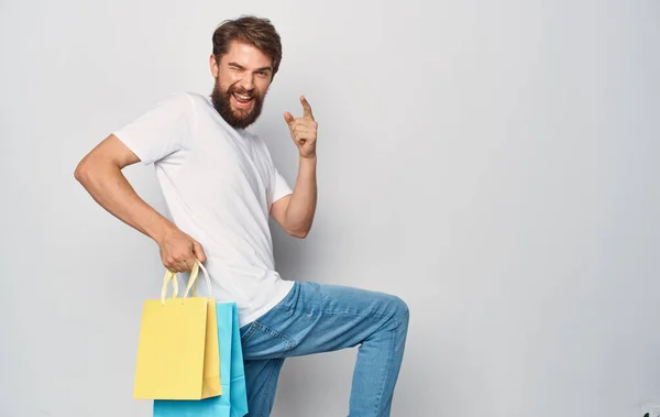 Человек в белой футболке и джинсах с пакетами в руках весело покупок радость изолированной фольги — стоковое фото
