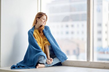 Ekoseli güzel bir kadın pencere eşiğinde oturur ve pencereden dışarı bakar.