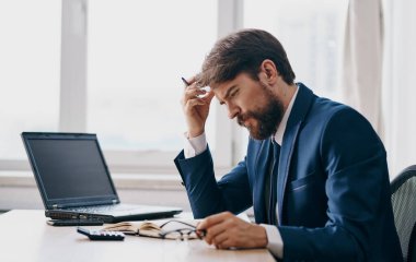 Klasik takım elbiseli bir adam masada oturur ve bir dizüstü bilgisayar ofis penceresi açık, şaşkın bir bakış.