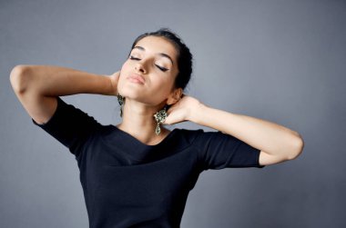 Güzel esmer, yüzünün yanında el ele tutuşuyor. Gece elbisesi odası gri duvar.