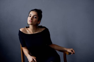 Gri bir odada, sandalyede oturan gece elbisesi içindeki zarif bayan yakın plan çekimleri yaptı.