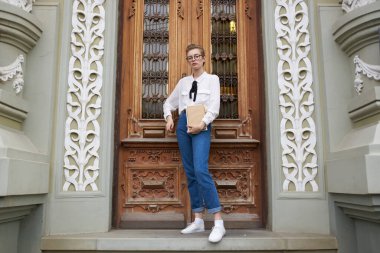 Gözlüklü güzel sarışın enstitü dış eğitim binasının kapısında duruyor.