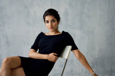 Kolunda bileziği olan seksi esmer kapalı bir sandalyede oturuyor.