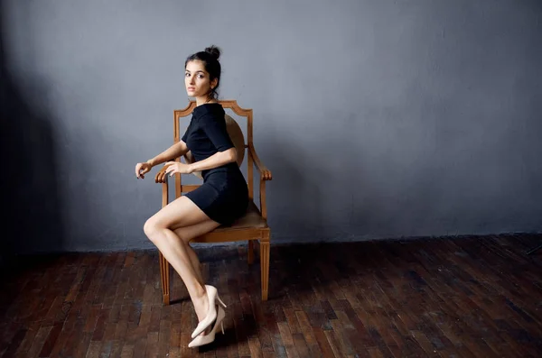 Σέξι μελαχρινή γυναίκα κάθεται σε μια καρέκλα σε εσωτερικούς χώρους σκουλαρίκια φόρεμα hairstyle μοντέλο — Φωτογραφία Αρχείου