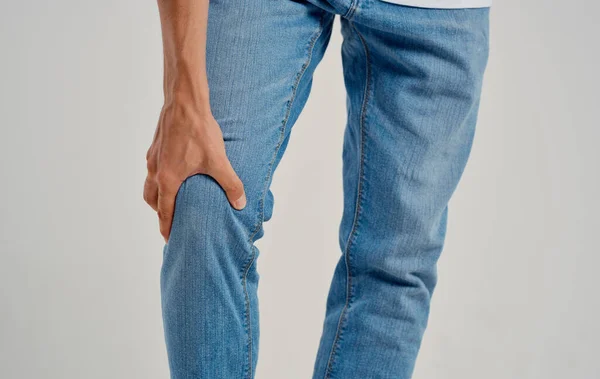 Homem de jeans toca seu joelho com as mãos em um fundo leve vista cortada — Fotografia de Stock