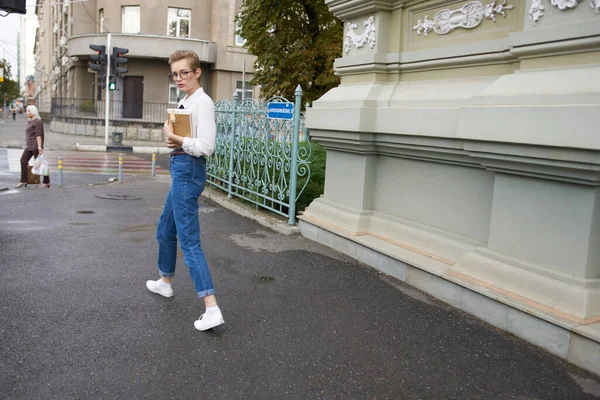 Vacker kvinna modell jeans med bok i handen nära byggnad på gatan — Stockfoto