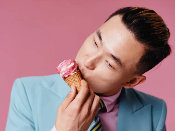アジア系の男が青いスーツピンクの背景でアイスクリームを食べるクローズアップ — ストック写真