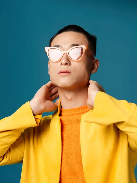 Chico sosteniendo sus manos detrás de su cabeza amarillo chaqueta asiático azul fondo — Foto de Stock