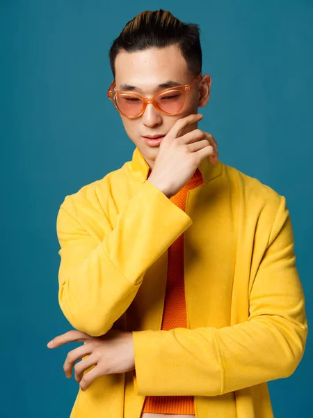 Hombre asiático con chaqueta amarilla sobre fondo azul y gafas en la cara, peinado — Foto de Stock