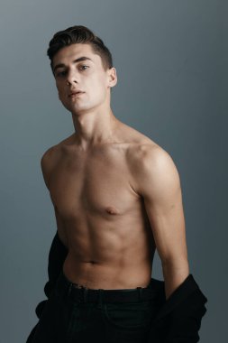 Çıplak omuzlu, koyu renk elbiseli, gri arka planlı bir adam.