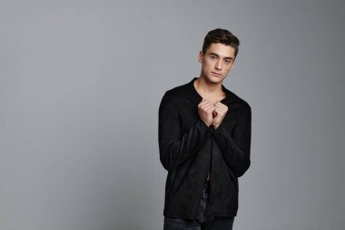 Koyu takım elbiseli zarif bir beyefendi. Gri arka planda el kol hareketi yapıyor.