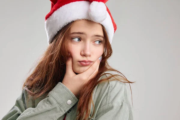 Triste fille dans un chapeau de Noël touche son visage avec sa main et regarde vers le côté — Photo