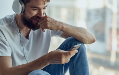 Kulaklıklı neşeli adam pencere eşiğinde müzik dinliyor.