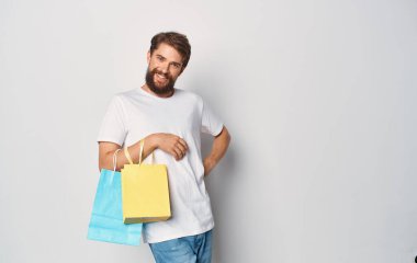 Beyaz tişörtlü bir adamın elinde çok renkli paketler var.