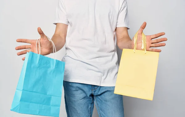 Paquetes multicolores en las manos de un hombre blanco camiseta estudio de compras — Foto de Stock