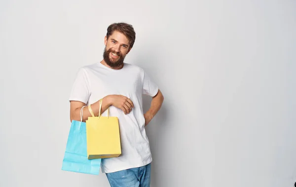 Sokszínű csomagok egy férfi fehér póló bevásárló stúdió kezében — Stock Fotó