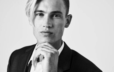 Çekici bir adam yüzünün yanında el ele tutuşuyor ve şaşkın görünüyor. Gri fotoğraf.