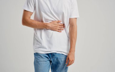 Beyaz tişörtlü ve kot pantolonlu bir adam elleriyle karnına dokunuyor.