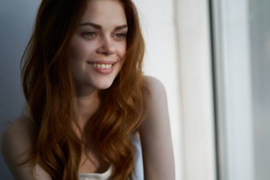 Sabah dinlenirken pencerenin yanında gülümseyen güzel kadın.