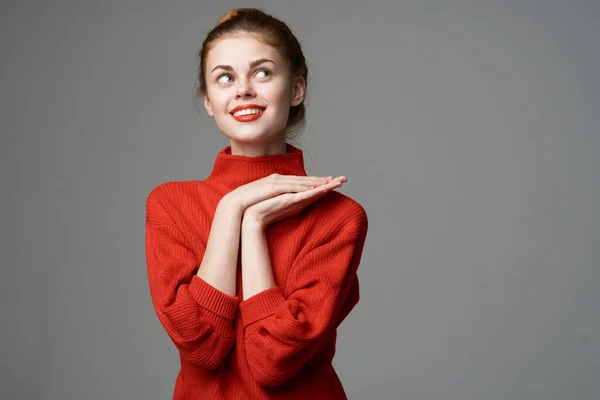 Ευτυχισμένη γυναίκα με κόκκινο πουλόβερ σε γκρι φόντο χειρονομίες με τα χέρια της συναισθήματα ιδέα ονειροπόληση — Φωτογραφία Αρχείου