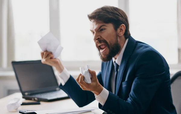 Homme d'affaires agressif dans un costume avec des feuilles de papier blanc dans ses mains dans le bureau près de la fenêtre — Photo