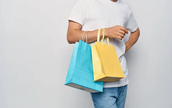 Paquetes multicolores en las manos de un hombre blanco camiseta estudio de compras — Foto de Stock