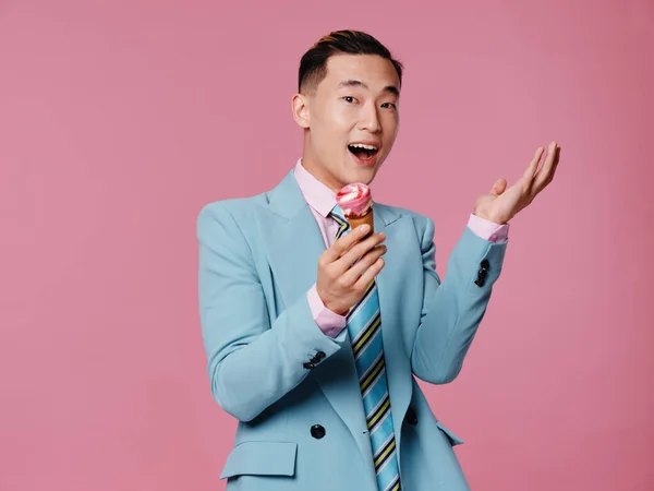 Man of Asian appearance in blue suit ice cream joy pink background — Stock Photo, Image