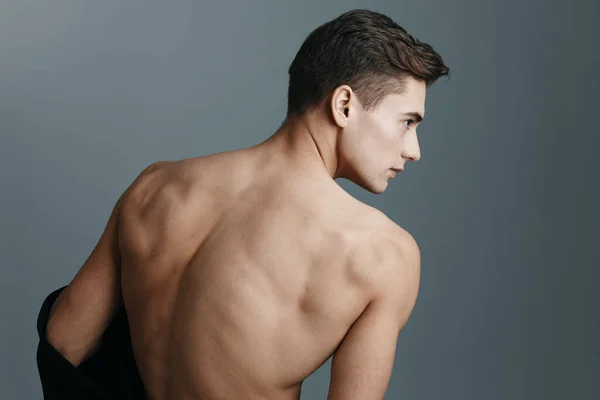 Homem sexy com costas nuas olha para o lado em um fundo cinza visão traseira de um esporte fitness — Fotografia de Stock
