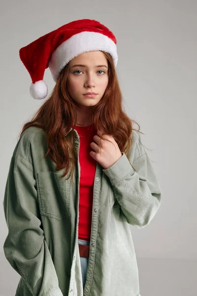 Gri bir arka planda Noel şapkalı ve kalın bir ceket giyen bir kızın portresi. — Stok fotoğraf