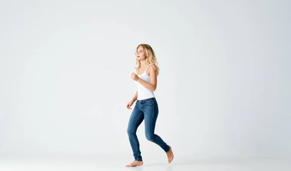 Una mujer delgada en jeans y una camiseta blanca descalza sobre un fondo claro en pleno crecimiento —  Fotos de Stock