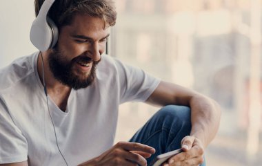 Kulaklıklı neşeli adam pencere eşiğinde müzik dinliyor.